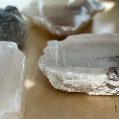 Angled close-up view: multiple alabaster stone trays, with a gray and white tray in focus.