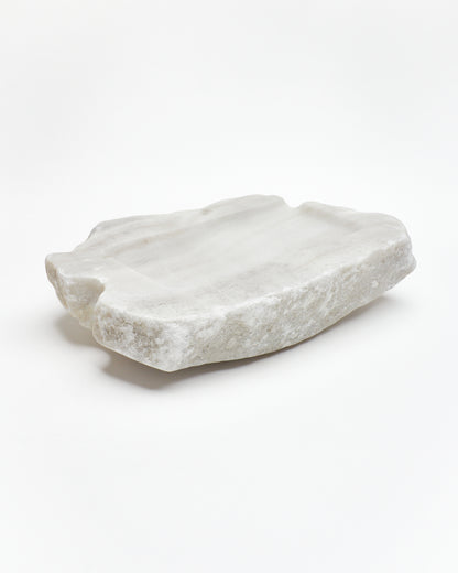 Angled back: organic-rectangle off-white alabaster tray with raw edges, flecks, semicircle cutout.