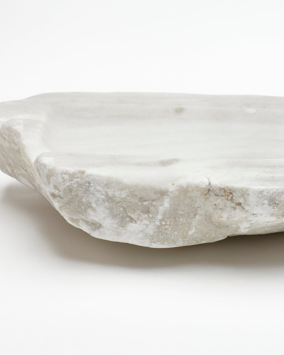 Close-up side view: off-white alabaster sculpture with raw edges, subtle marks, and flecks.