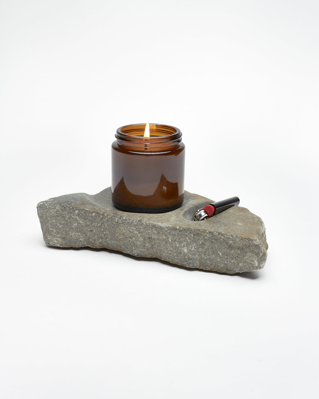 Side: gray stone sculpture, raw edges, carved spaces for—and holding—lighter and jar candle. 