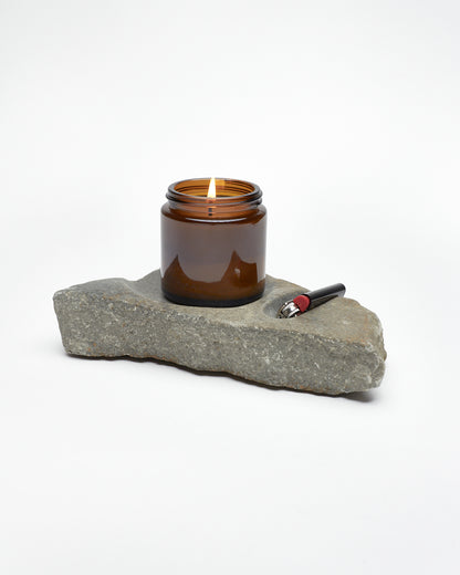 Side: gray stone sculpture, raw edges, carved spaces for—and holding—lighter and jar candle. 