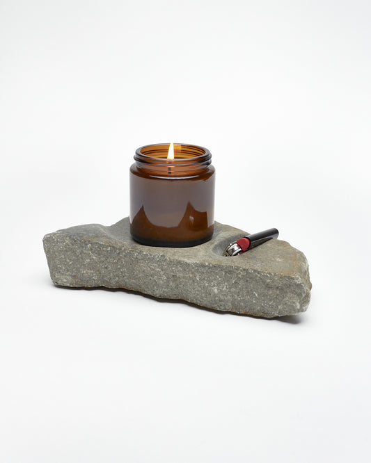 Side: gray stone sculpture, raw edges, carved spaces for—and holding—lighter and jar candle. 