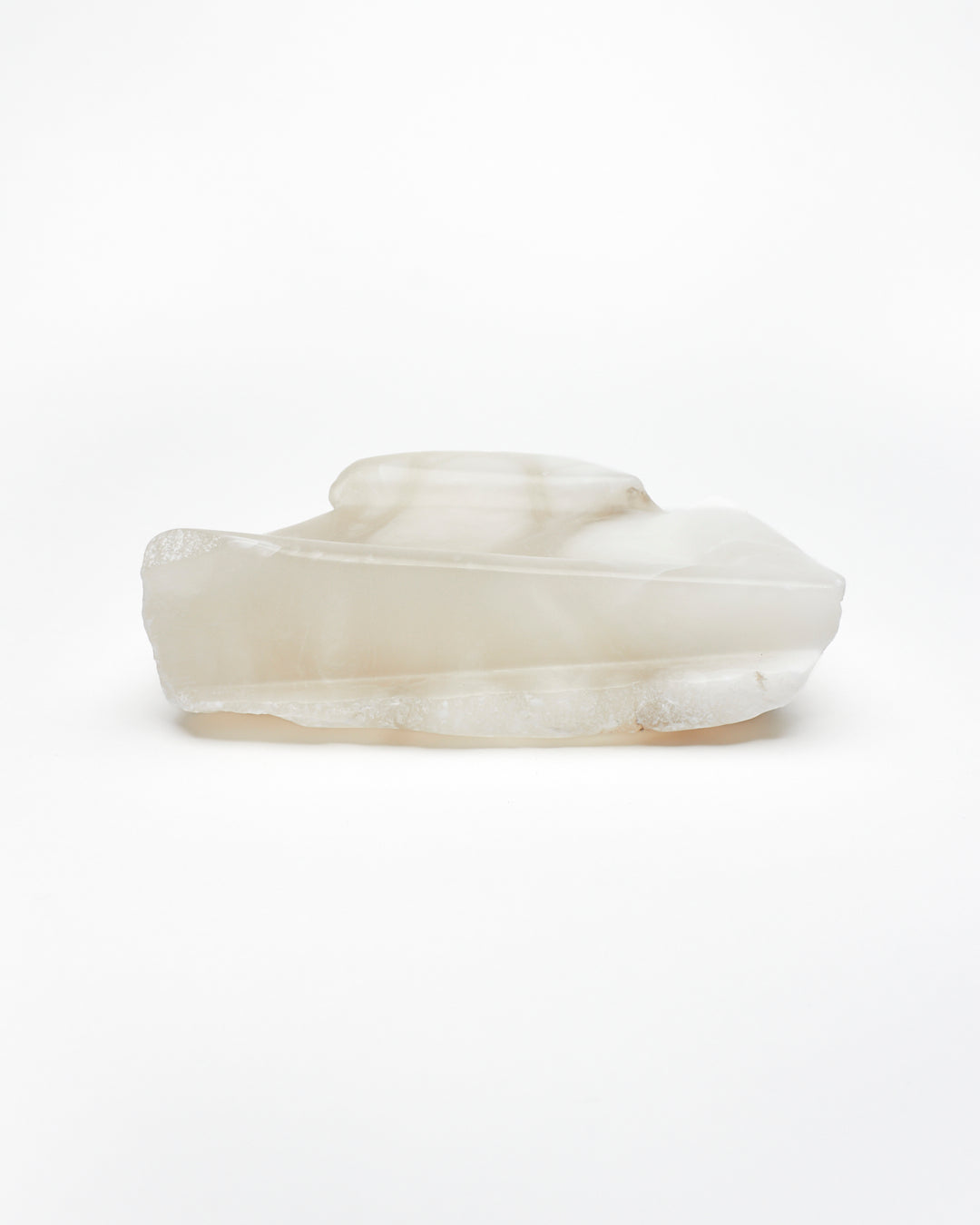 Side view: white translucent alabaster tray with raw and smooth edges.