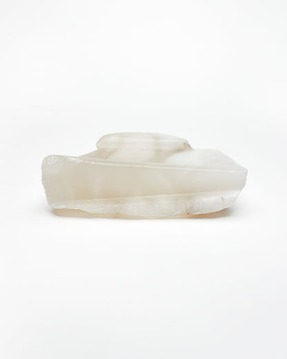 Side view: white translucent alabaster tray with raw and smooth edges.
