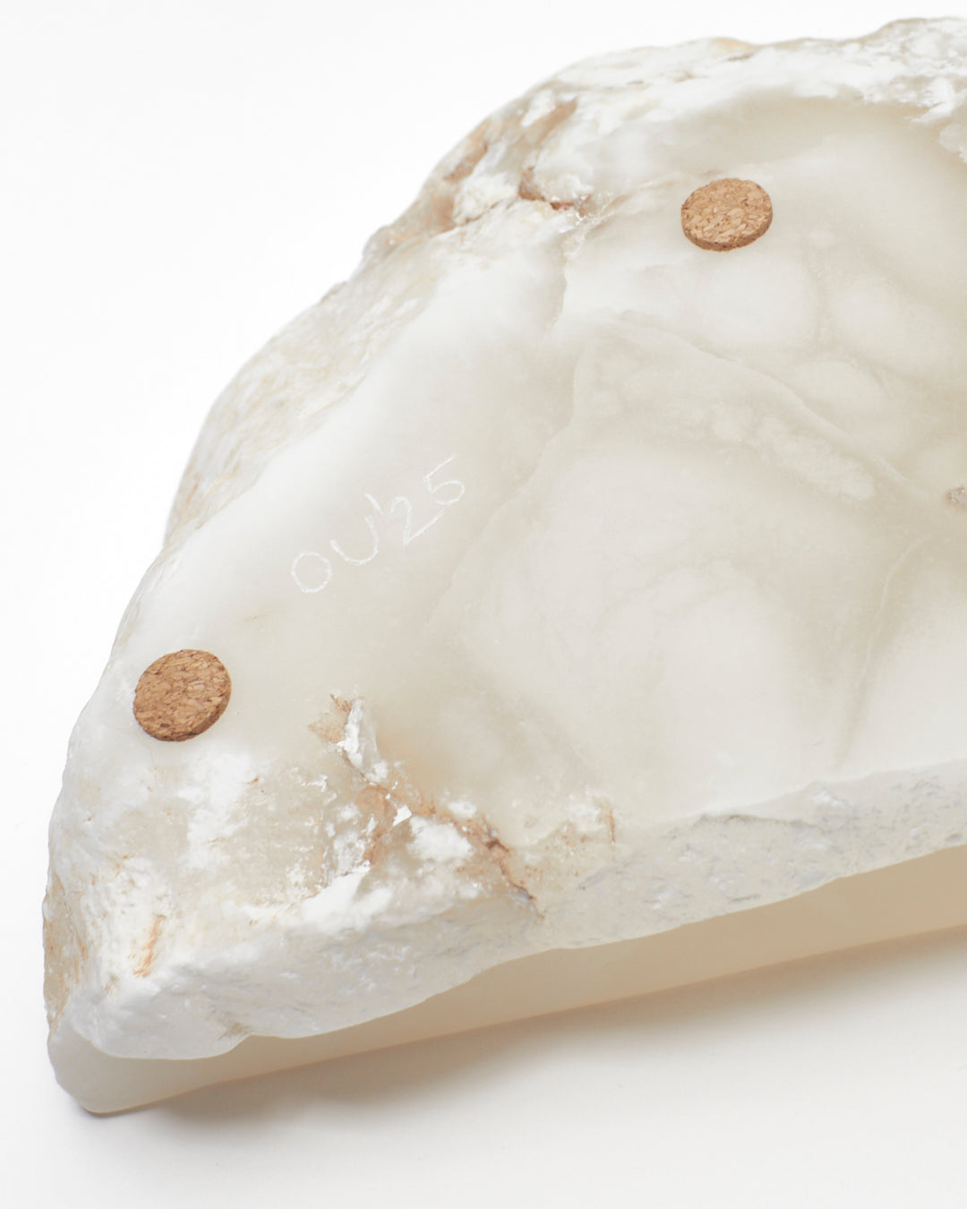 Underside close-up view: white translucent alabaster tray with flecks, cork pads, OU’25 engraving.