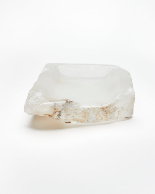 Front view: white translucent alabaster tray with raw and smooth edges, brown veining, cork pads.