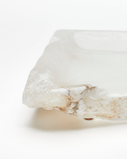 Front-on close-up: white translucent alabaster tray with raw edge, brown veining, cork pad.