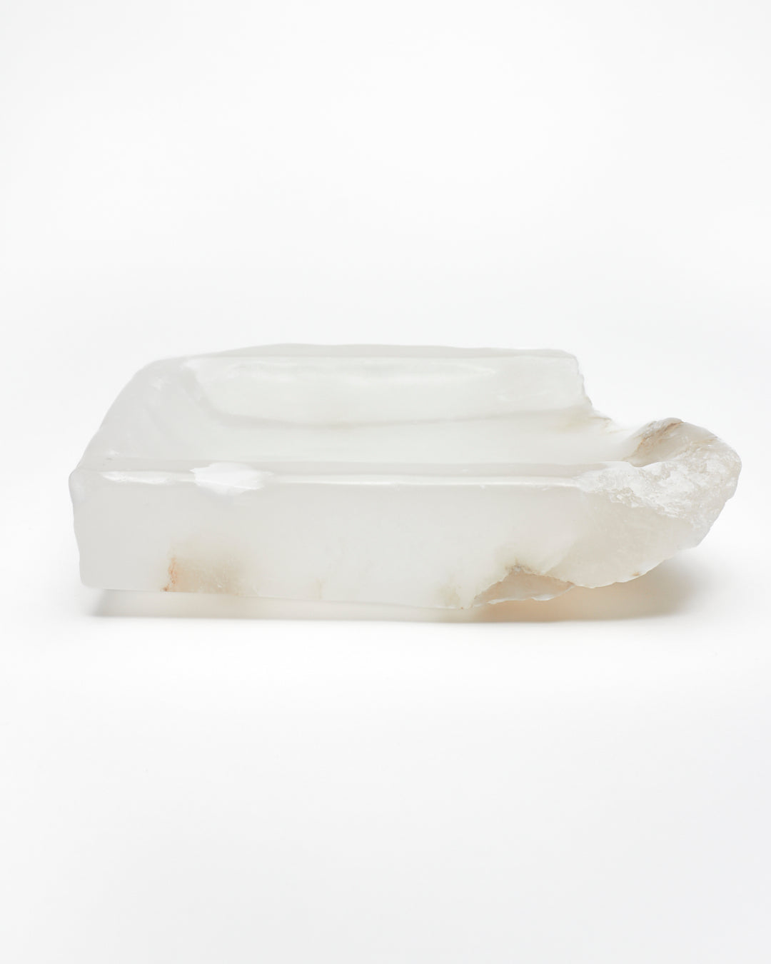 Side view: white translucent alabaster tray with raw and smooth edges and brown veining.