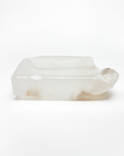Side view: white translucent alabaster tray with raw and smooth edges and brown veining.