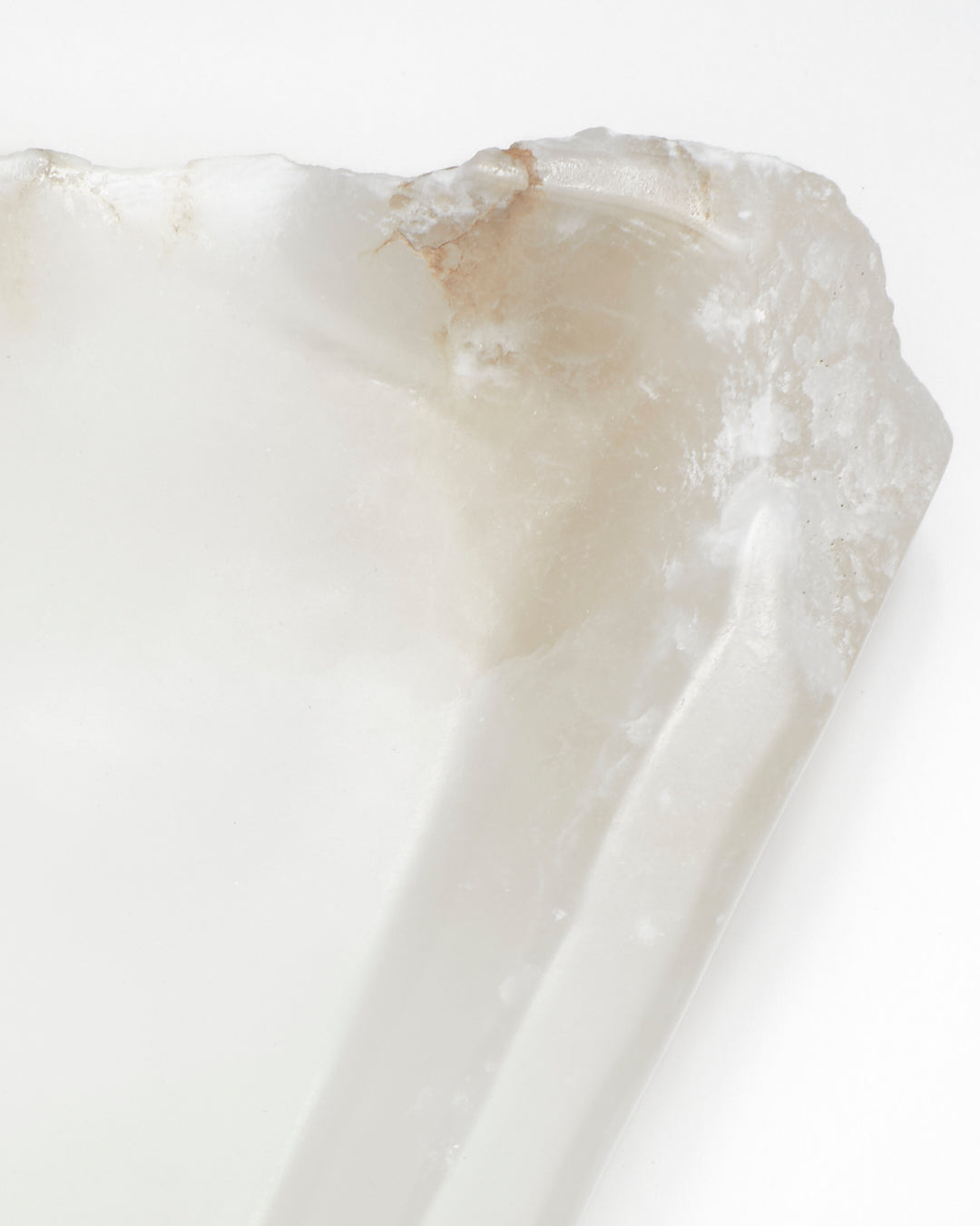Top-down close-up: white translucent alabaster tray with raw and smooth edges, brown veining.