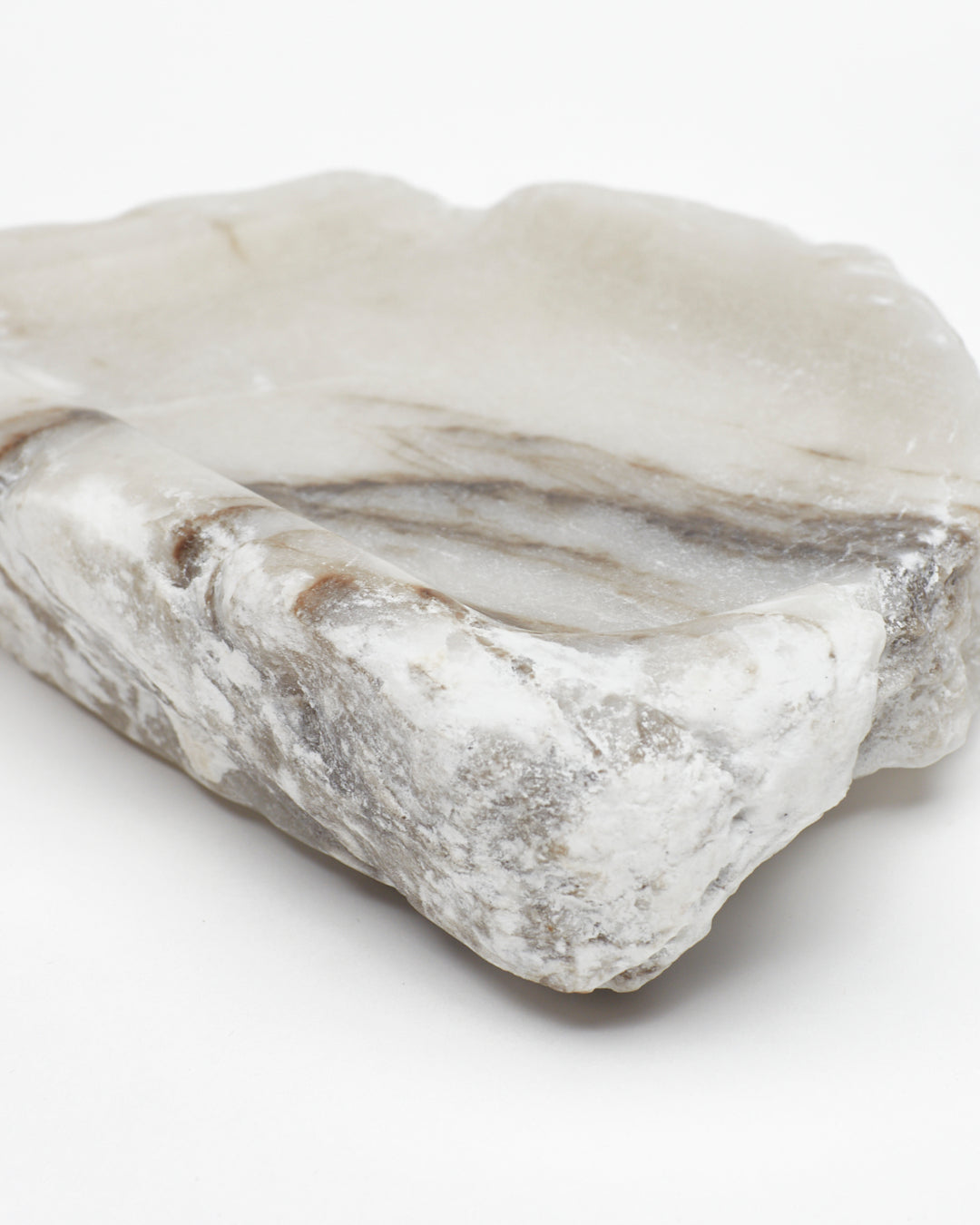 Angled close-up view: organic-shaped white alabaster tray, dark streaks, and raw edges.