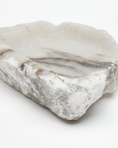 Angled close-up view: organic-shaped white alabaster tray, dark streaks, and raw edges.