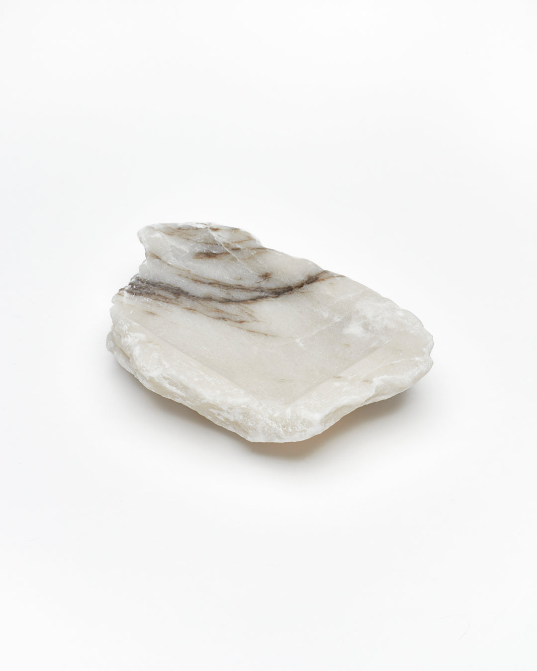 Angled back view: organic-shaped white alabaster tray, dark streaks, and raw edges.