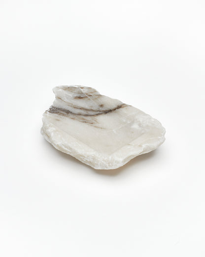 Angled back view: organic-shaped white alabaster tray, dark streaks, and raw edges.
