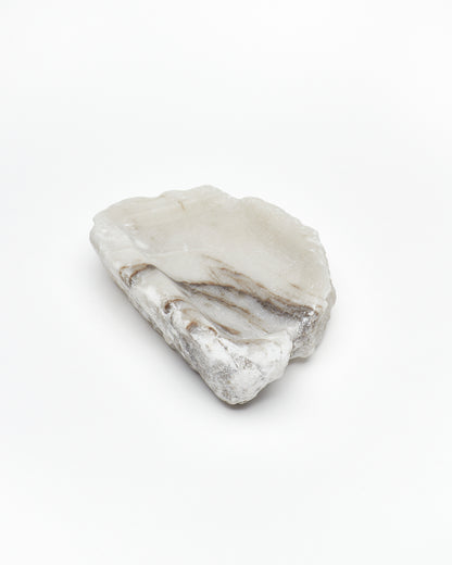 Angled view: organic-shaped white alabaster tray, dark streaks, and raw edges.