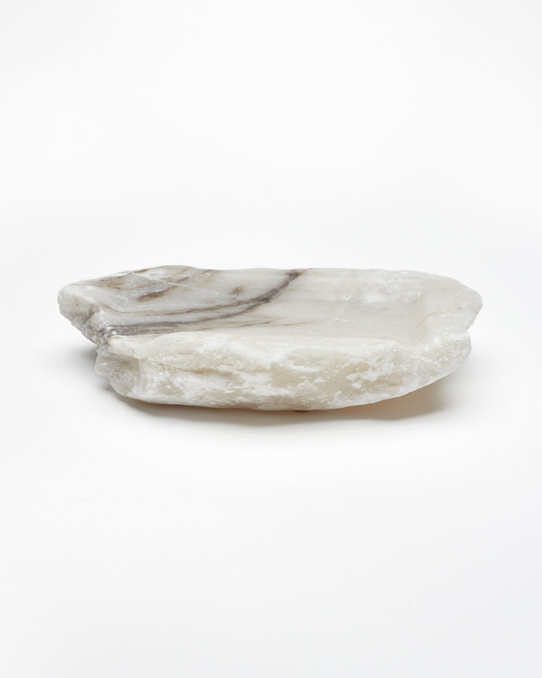 Side view: organic-shaped white alabaster tray, dark streaks, and raw edges.