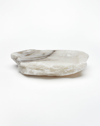 Side view: organic-shaped white alabaster tray, dark streaks, and raw edges.