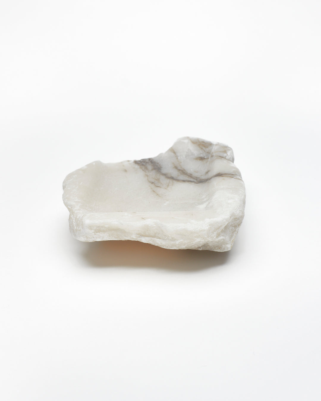 Back view: organic-shaped white alabaster tray, dark streaks, and raw edges.