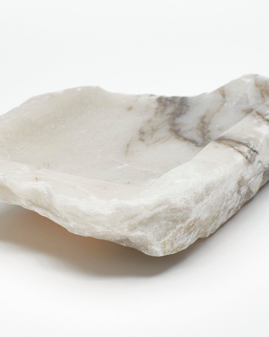 Angled back close-up: organic-shaped white alabaster tray, dark streaks, and raw edges.