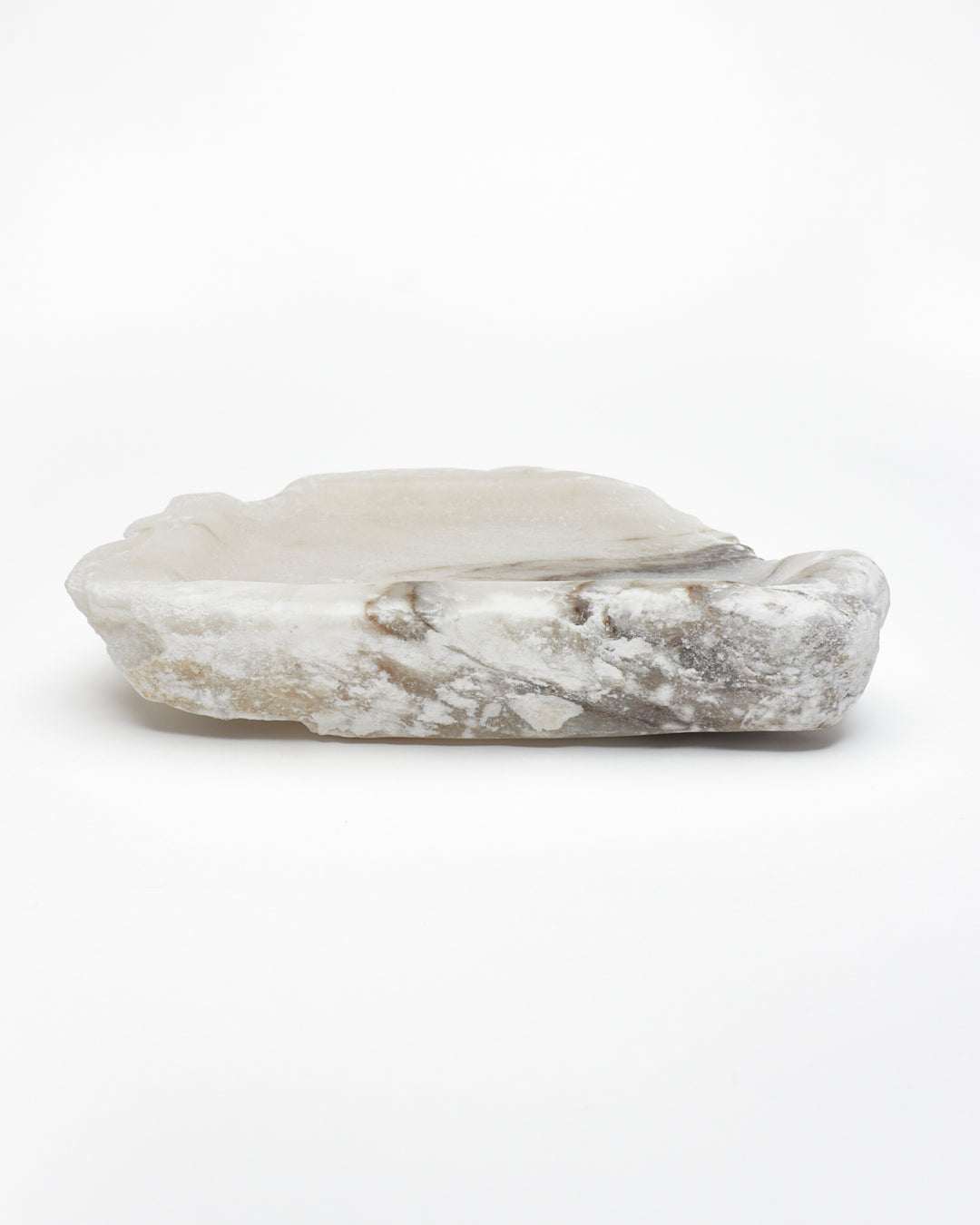 Side view: organic-shaped white alabaster tray, dark streaks, and raw edges.