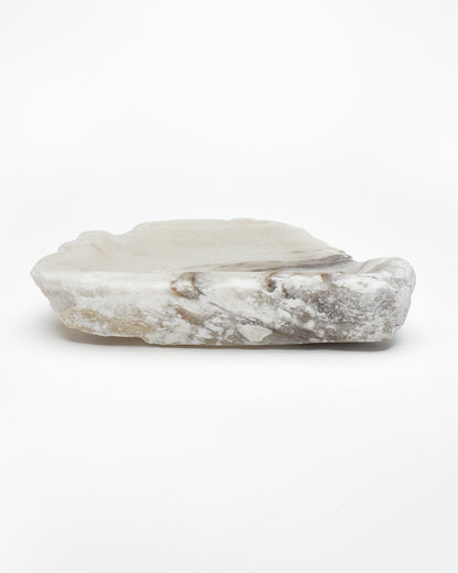 Side view: organic-shaped white alabaster tray, dark streaks, and raw edges.