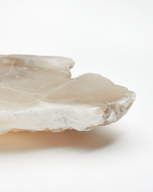 Close-up side view: organically shaped tan and white alabaster tray, brown flecks, raw edges.