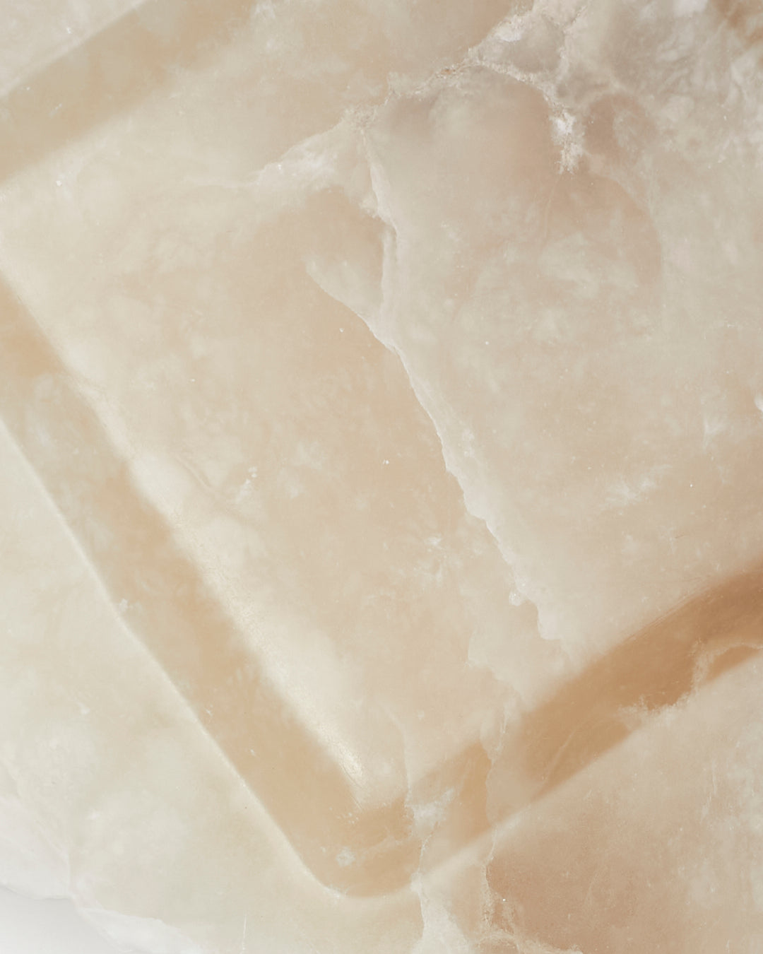 Top-down close-up: tan and cream alabaster tray surface with veining.