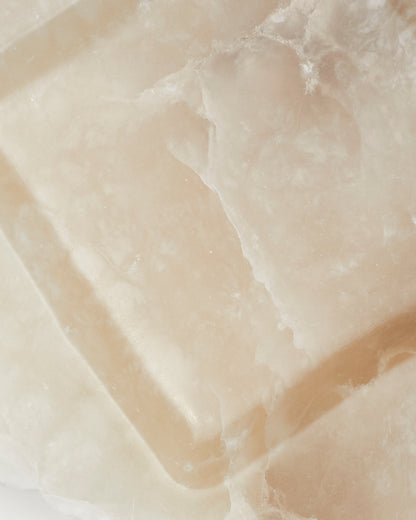 Top-down close-up: tan and cream alabaster tray surface with veining.