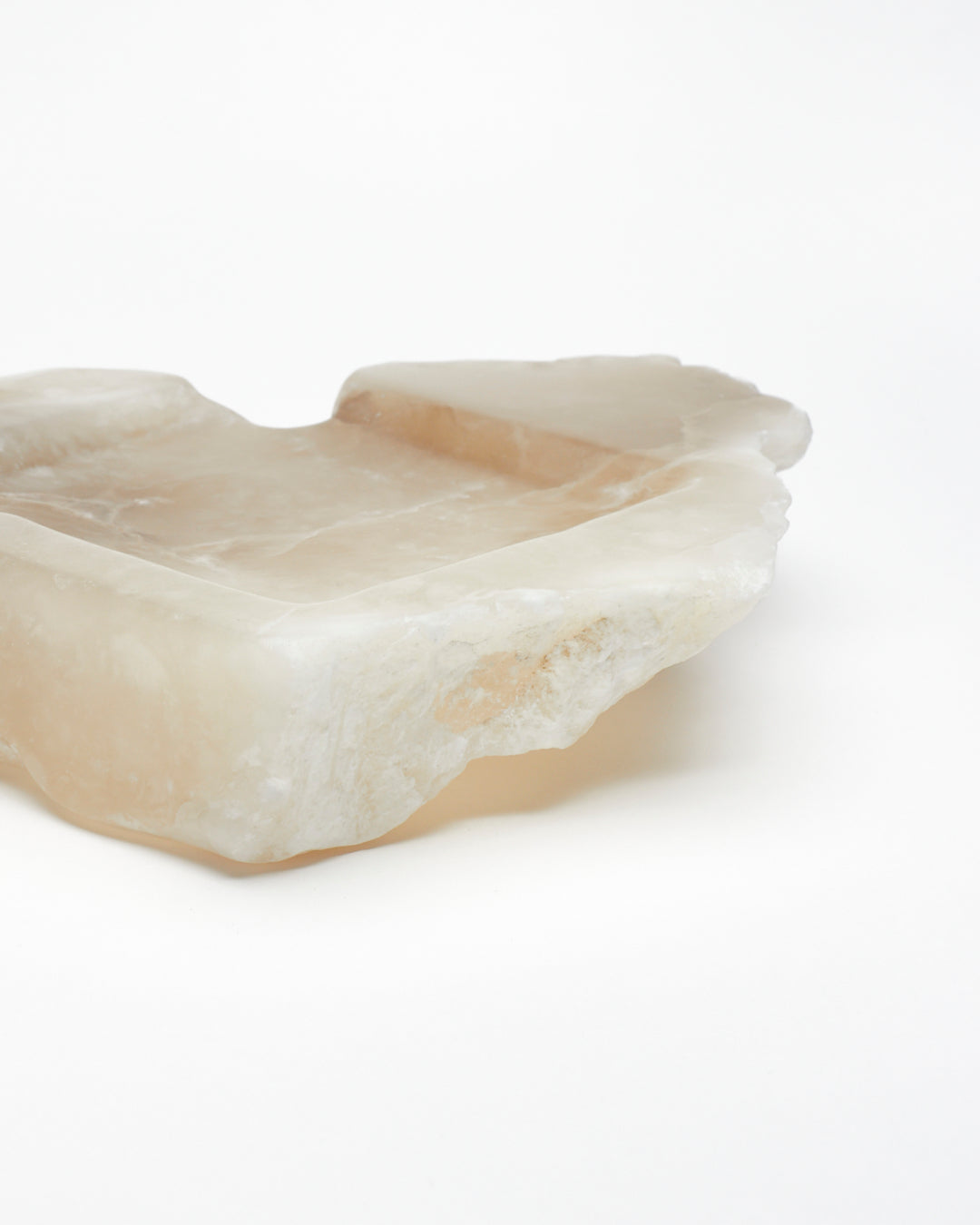 Close-up side view: organically shaped, tan and white alabaster tray with raw edges.