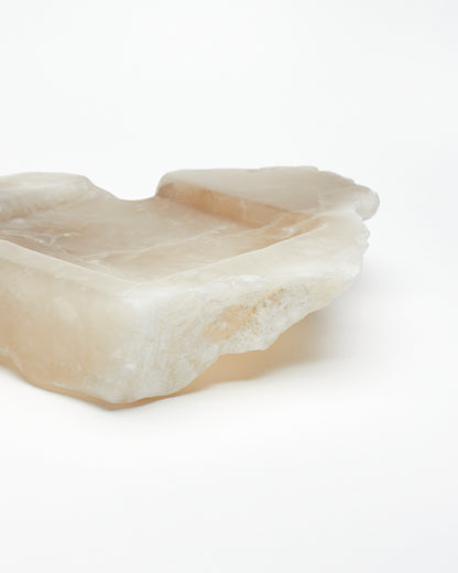 Close-up side view: organically shaped, tan and white alabaster tray with raw edges.