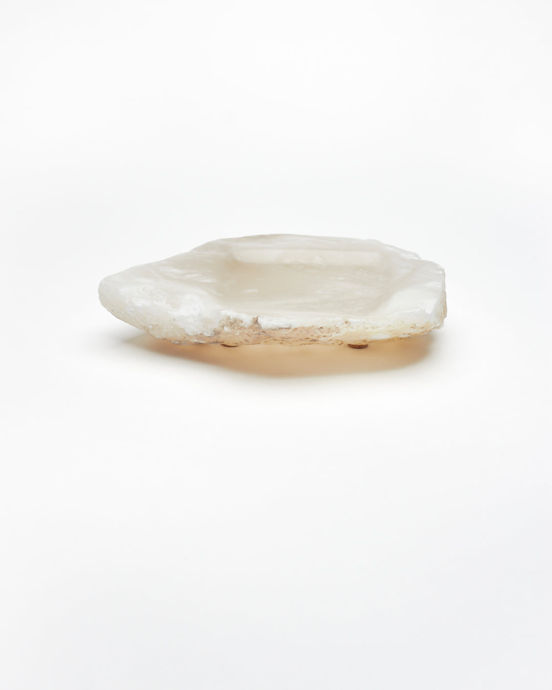 Side view: organic-shaped white translucent alabaster tray, brown flecks, raw edges, cork pads.