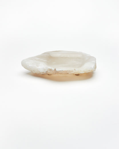 Side view: organic-shaped white translucent alabaster tray, brown flecks, raw edges, cork pads.