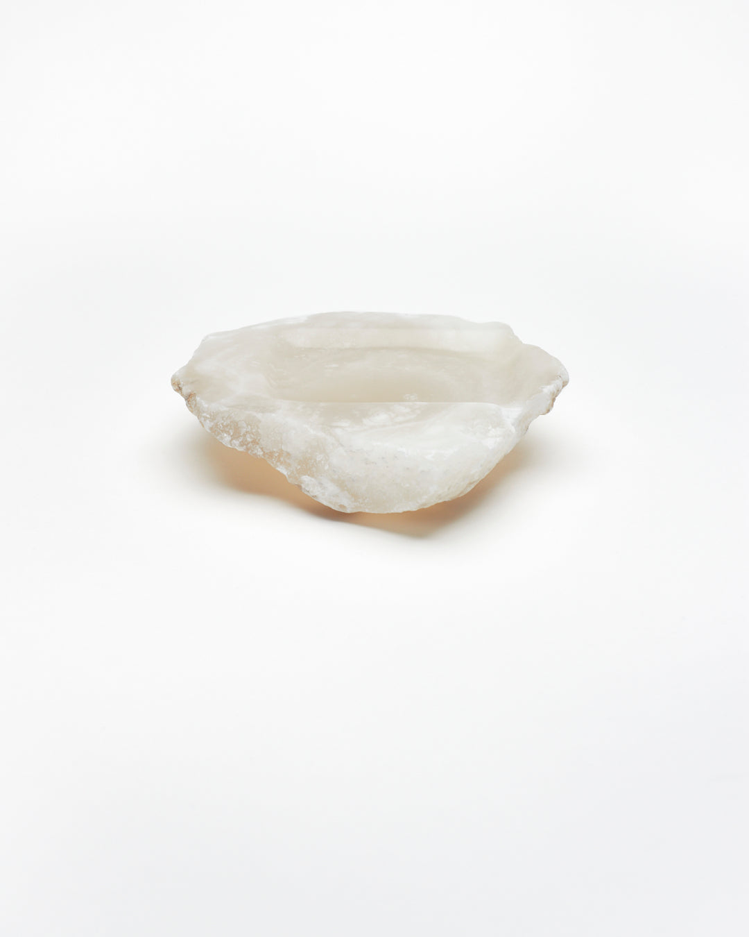 Side view: organic-shaped white translucent alabaster tray with raw edges.