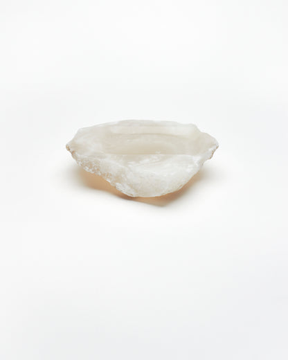 Side view: organic-shaped white translucent alabaster tray with raw edges.