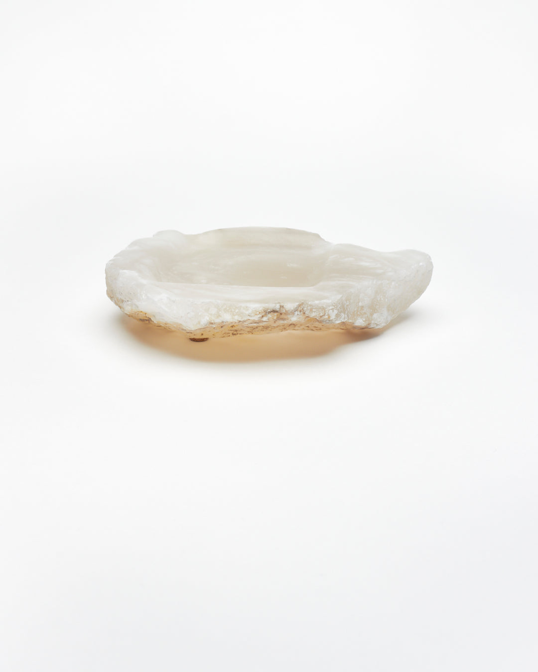 Side view: organic-shaped white translucent alabaster tray, brown flecks, raw edges, cork pads.
