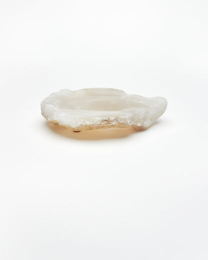 Side view: organic-shaped white translucent alabaster tray, brown flecks, raw edges, cork pads.