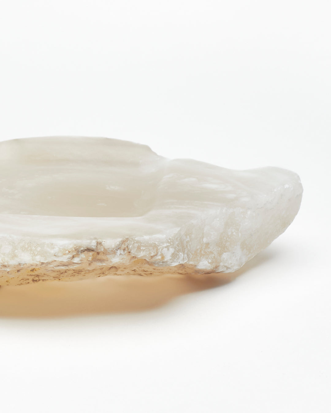 Close-up side view: organic-shaped white translucent alabaster tray, brown flecks, raw edges.