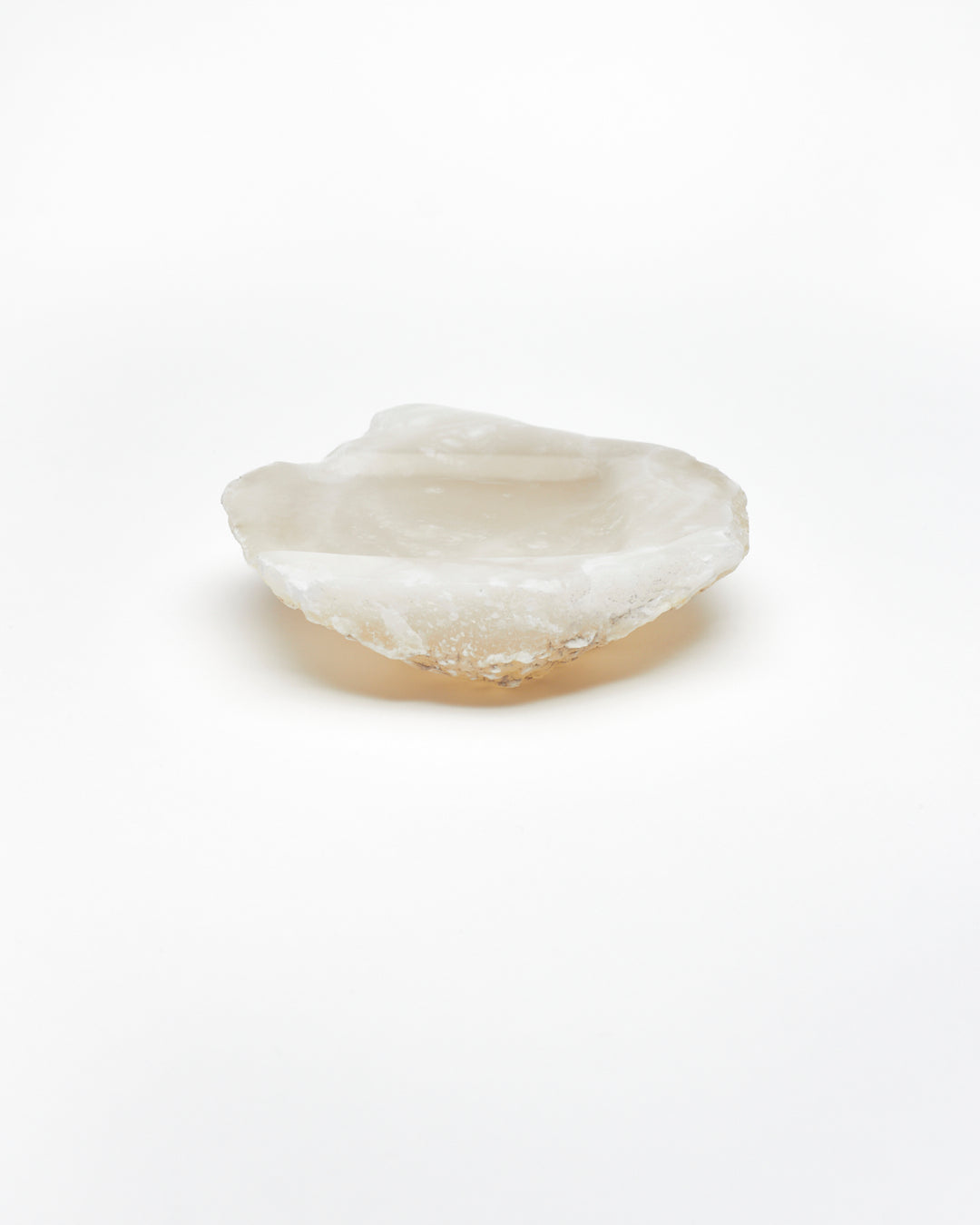 Side view: organic-shaped white translucent alabaster tray, brown flecks, raw edges.