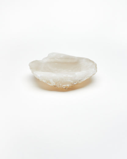 Side view: organic-shaped white translucent alabaster tray, brown flecks, raw edges.