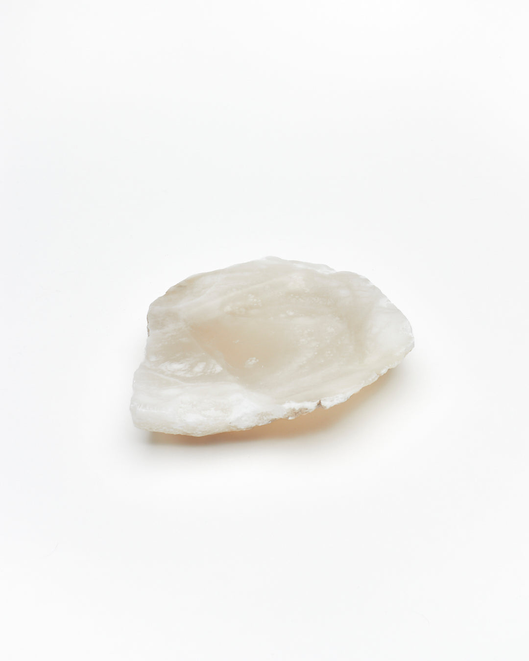 Angled view: organic-shaped white translucent alabaster tray, brown flecks, and raw edges.