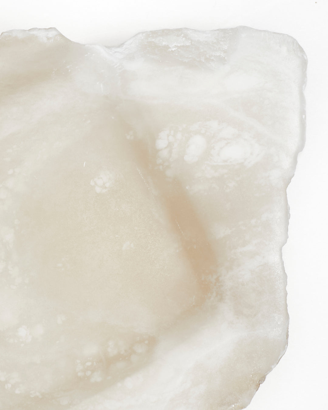 Top-down close-up: organically shaped, white translucent alabaster tray with raw edges.