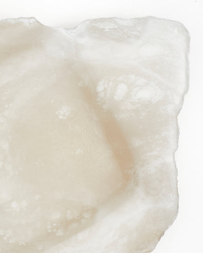 Top-down close-up: organically shaped, white translucent alabaster tray with raw edges.