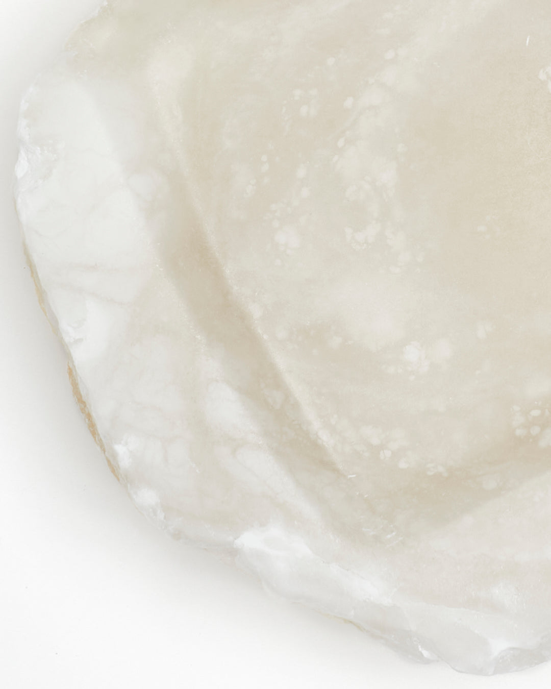 Top-down close-up: organically shaped, white translucent alabaster surface with raw edges.