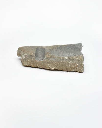Side view: organic-shaped gray-brown stone sculpture, raw edges, round and oval carvings.
