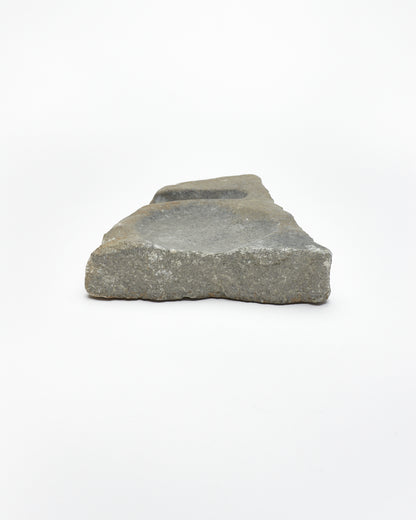 Back view: organic-shaped gray stone sculpture, raw edges, round and oval carvings.