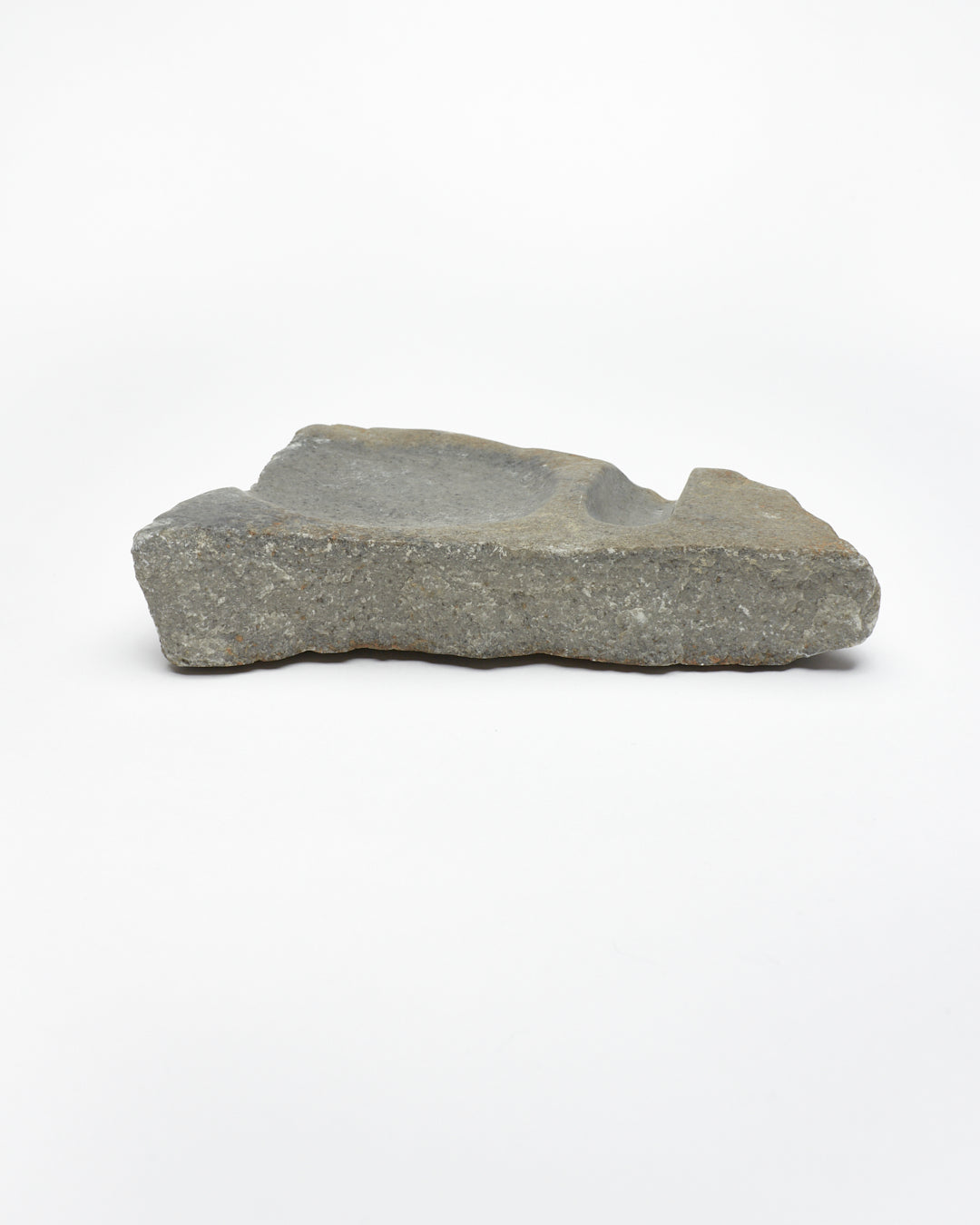Side view: organic-shaped gray stone sculpture, raw edges, round and oval carvings.