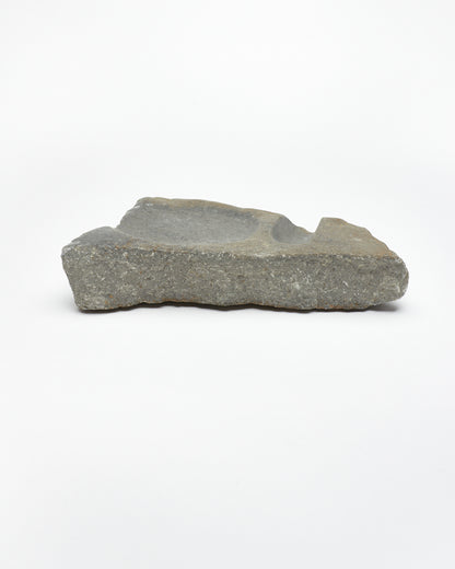 Side view: organic-shaped gray stone sculpture, raw edges, round and oval carvings.