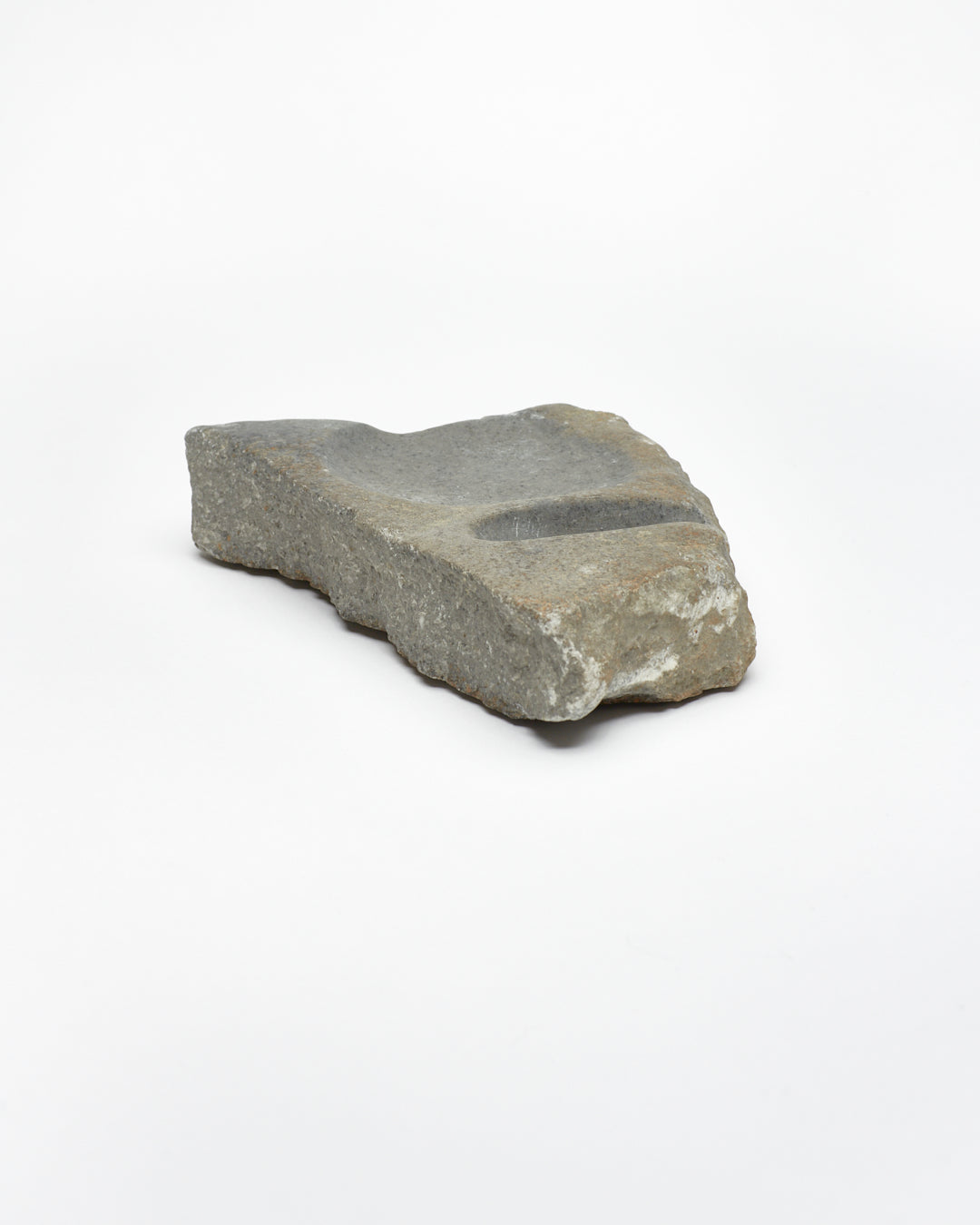 Angled view: organic-shaped gray-brown stone sculpture, raw edges, round and oval carvings.