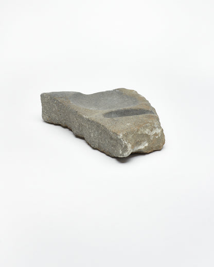 Angled view: organic-shaped gray-brown stone sculpture, raw edges, round and oval carvings.