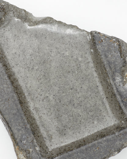 Top-down close-up: organic-shaped, gray stone tray with raw edges and a smooth surface.